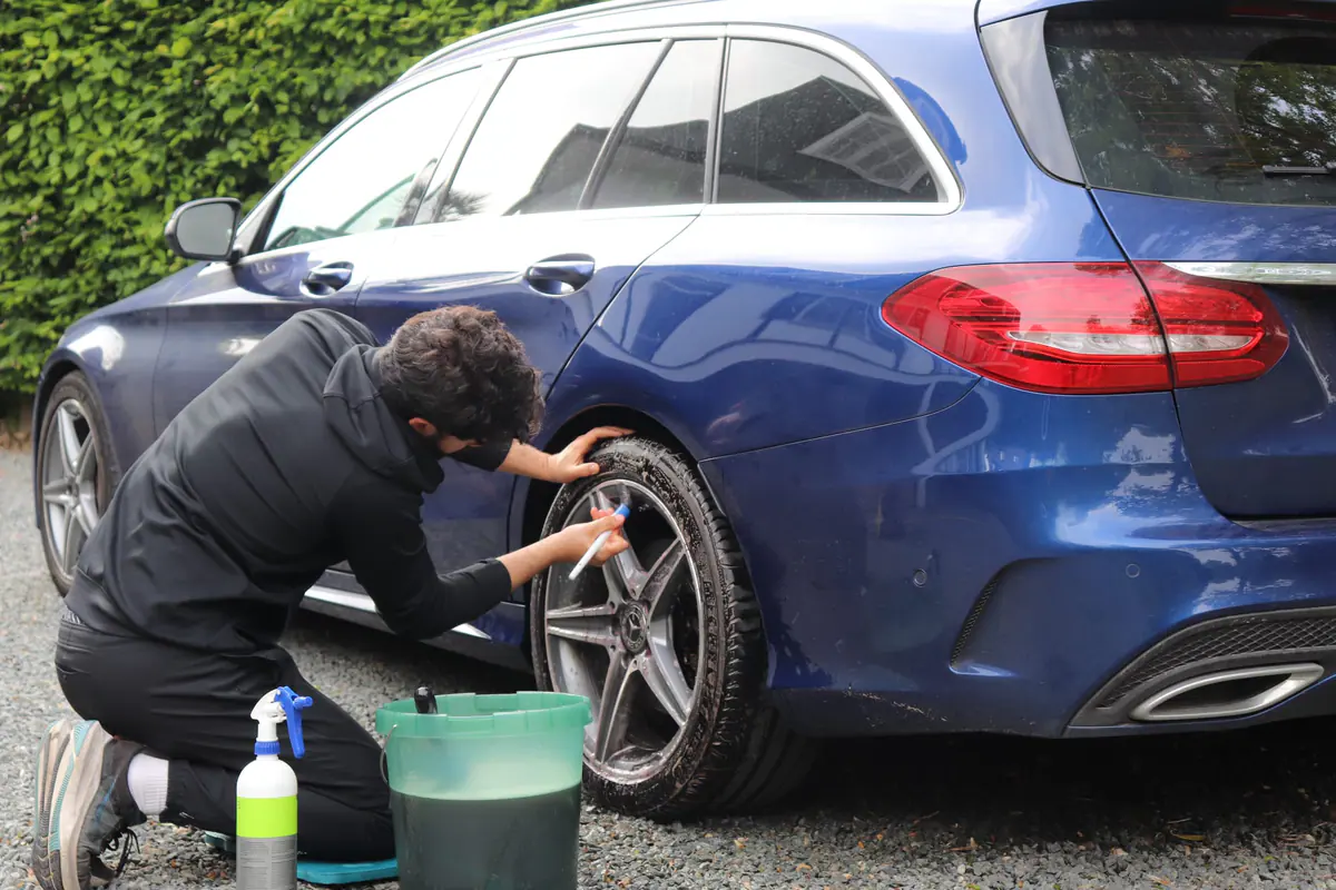 Iemand knielt bij het achterwiel van een donkerblauwe break en borstelt de velg schoon