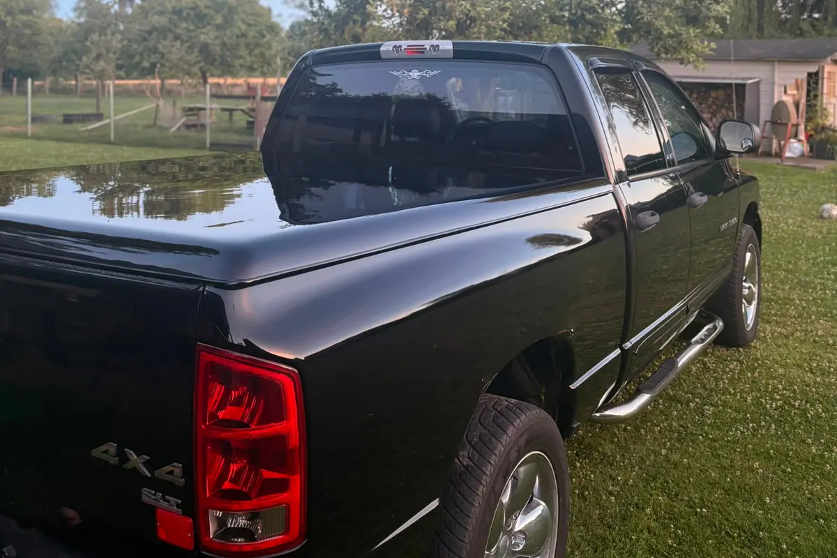 Dezelfde zwarte Dodge Ram pick-up staat op het gras bij een schuur, bomen spiegelen in de glanzende lak