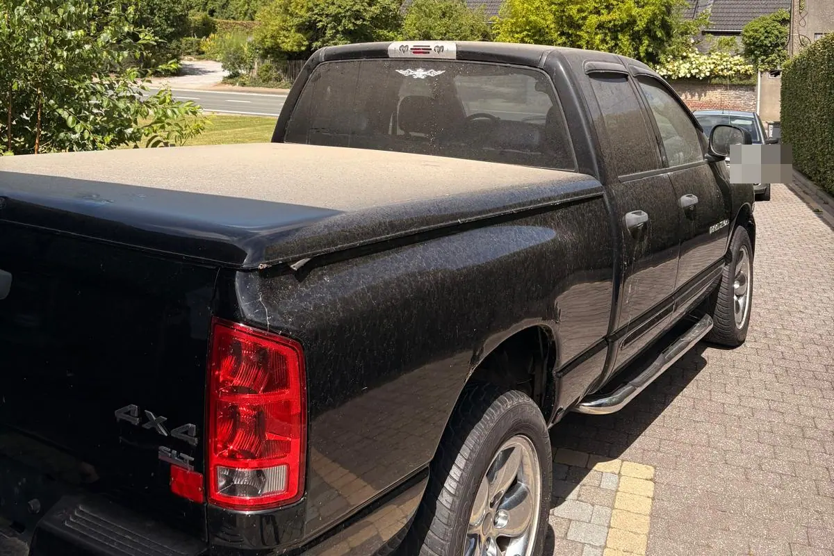Een zwarte Dodge Ram pick-up met dubbele cabine staat stoffig en vol droogvlekken op een klinkeroprit